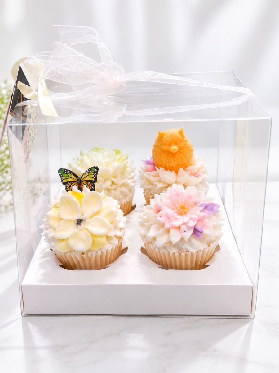 Box of four floral cupcakes with yellow blossom, pink lotus and orange puppy topper